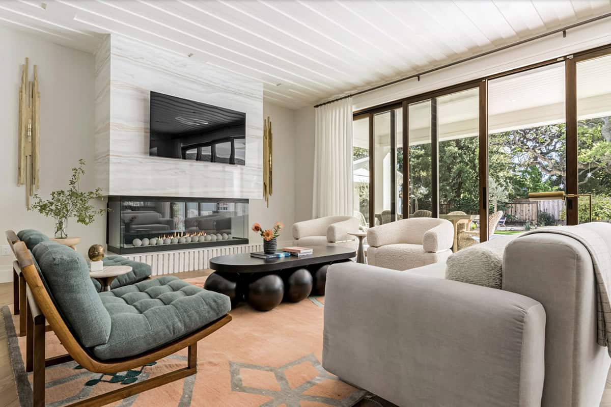 Family room with marble see-through fireplace, teal tufted chairs, bubble coffee table, and boucle armchairs