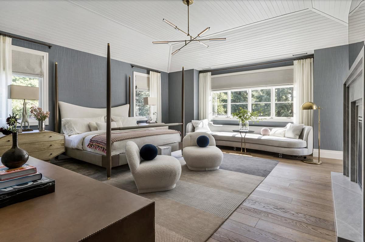 Primary bedroom with four-poster bed, slate blue grasscloth walls, boucle accent chairs, and sputnik chandelier