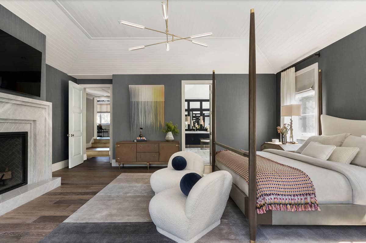 Primary bedroom with dark grasscloth walls, four-poster bed, marble fireplace, and brass sputnik ceiling light