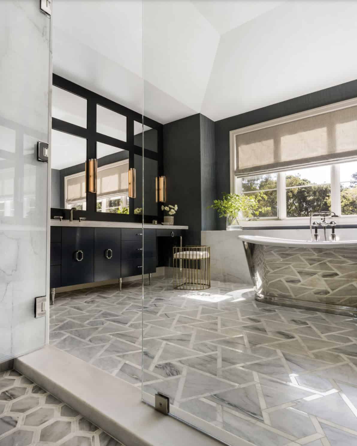 Primary bathroom with geometric marble mosaic floor, silver freestanding soaking tub, and navy vanity cabinets