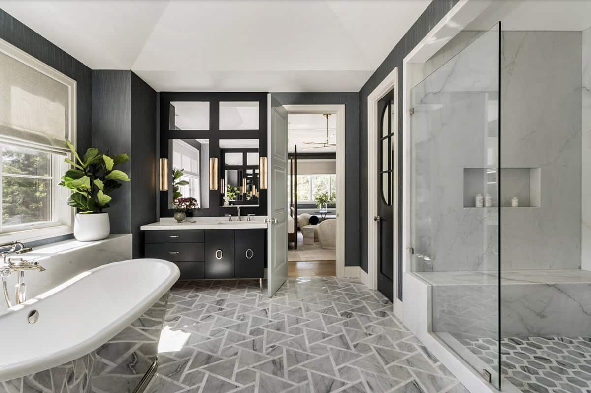 Primary bathroom with freestanding soaking tub, dark grasscloth walls, geometric marble tile floor, navy vanity, and glass-enclosed marble shower