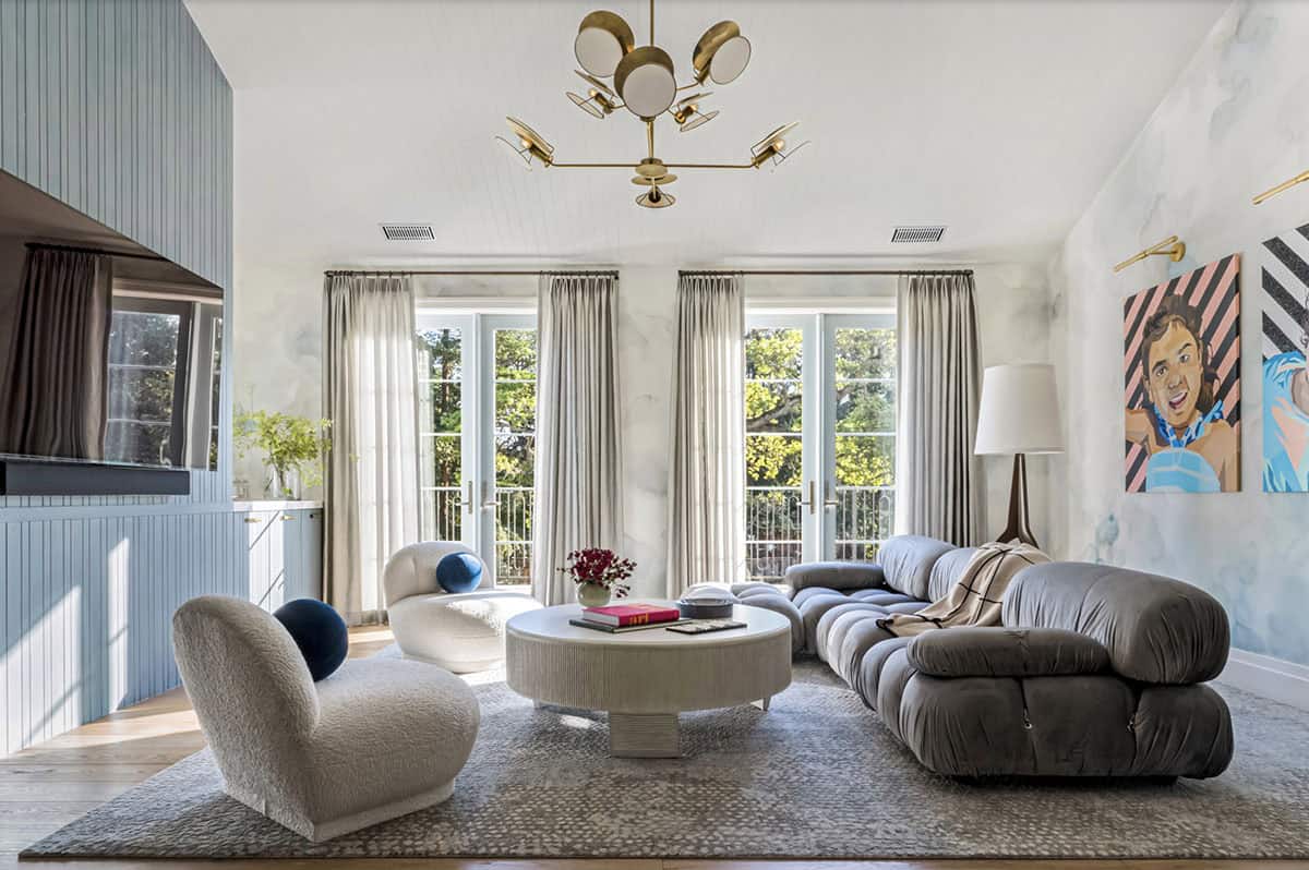 Upstairs lounge with segmented gray sofa, boucle accent chairs, brass chandelier, and watercolor-washed walls