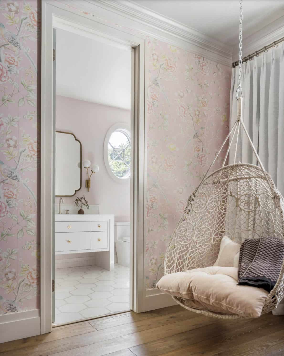 Girl's bedroom with pink chinoiserie wallpaper, macrame hanging chair, and view into en suite bathroom