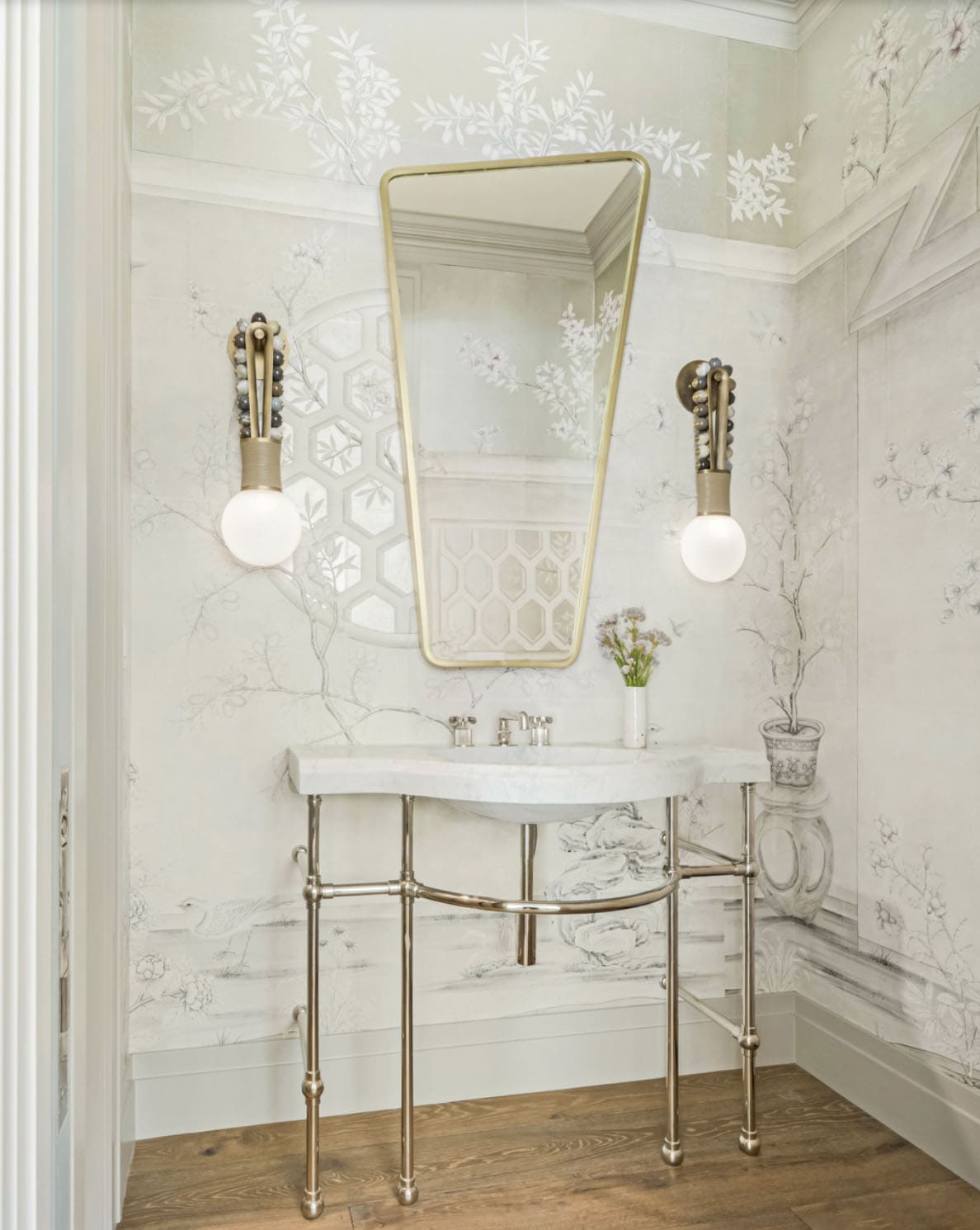 Bathroom with hand-painted chinoiserie mural wallpaper, marble console sink on polished nickel legs, and asymmetrical brass mirror