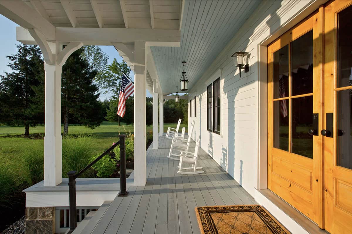 Wide farmhouse porch with pendant lanterns, gray decking, and natural wood entry doors