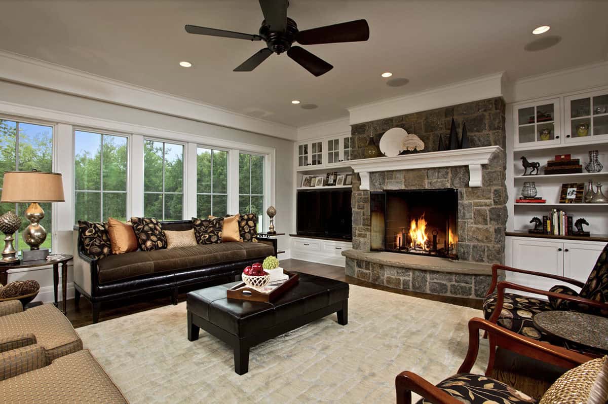 Living room with stone fireplace, built-in shelving, dark sofa, and large windows