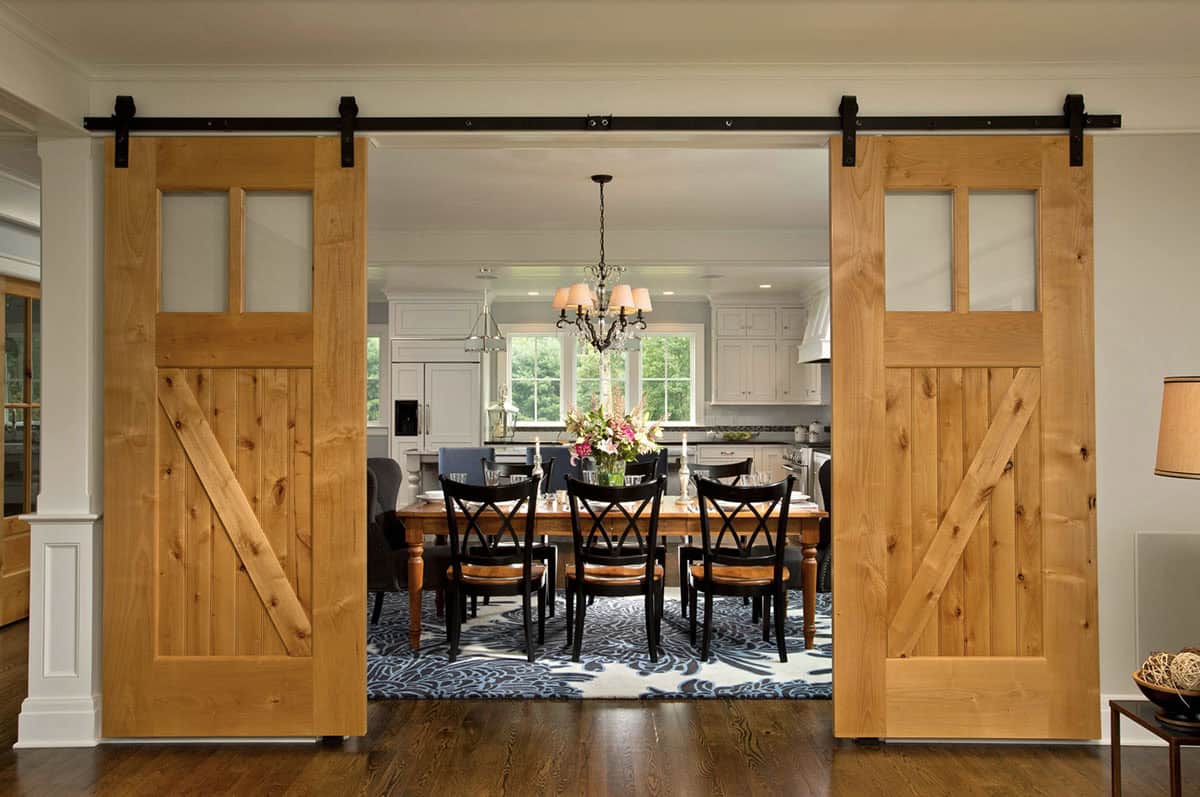 Sliding knotty alder barn doors opening to dining room with farm table and chandelier