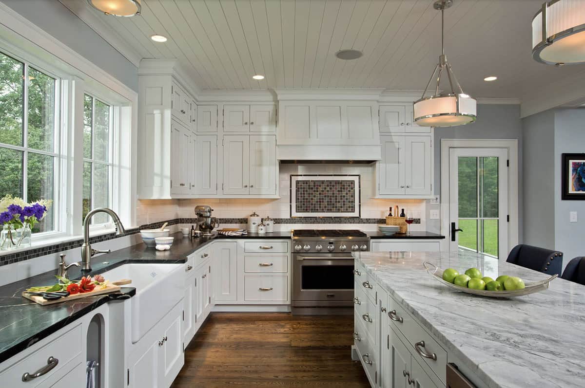 White farmhouse kitchen with black soapstone counters, farmhouse sink, and shiplap ceiling