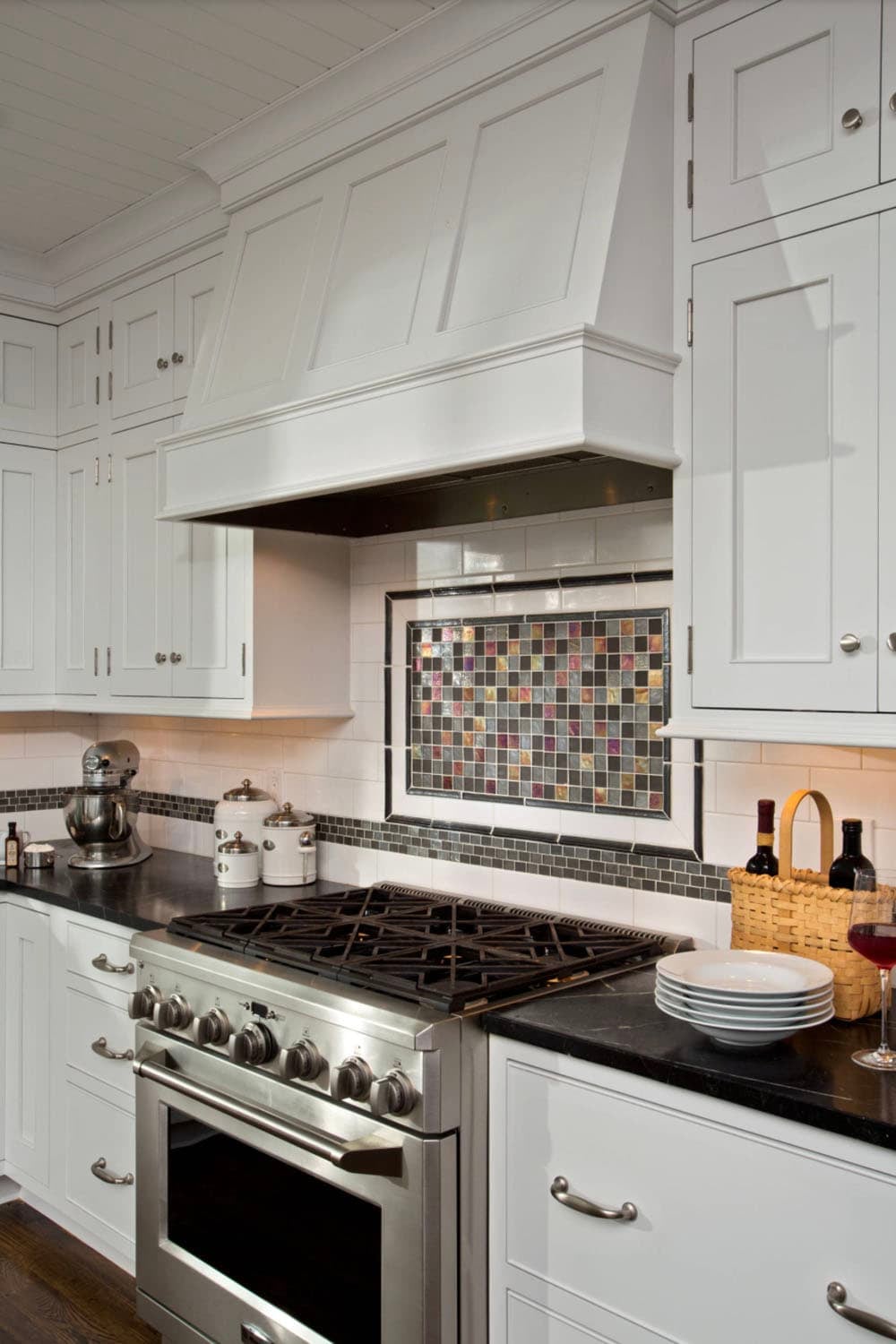 White kitchen range hood with mosaic tile backsplash and stainless steel range