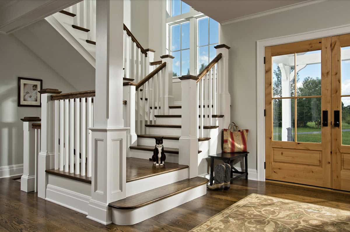 Foyer staircase with dark wood treads, white balusters, and knotty alder front door