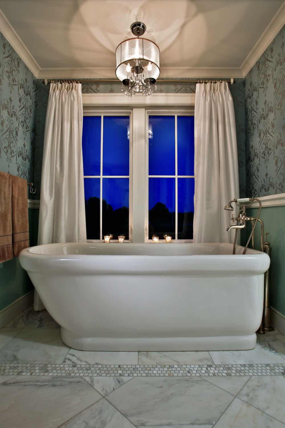 Primary bathroom with freestanding soaking tub, floral wallpaper, and crystal chandelier