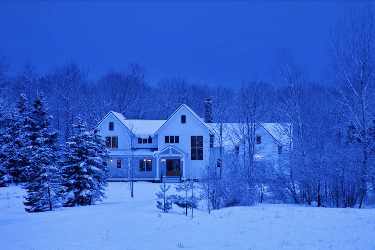 White farmhouse exterior at dusk surrounded by snow-covered trees in winter