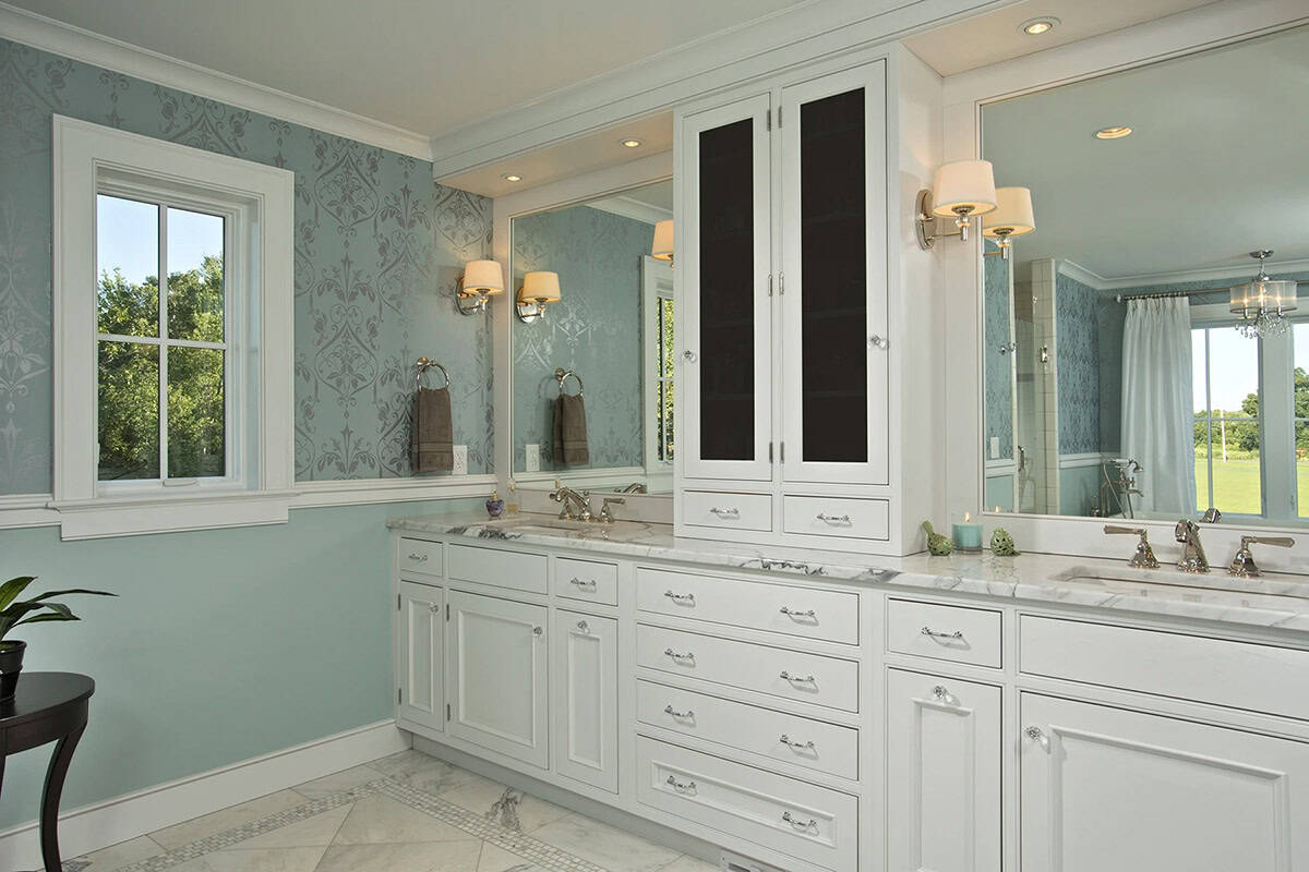 Primary bathroom double vanity with white cabinetry, marble countertops, and blue damask wallpaper