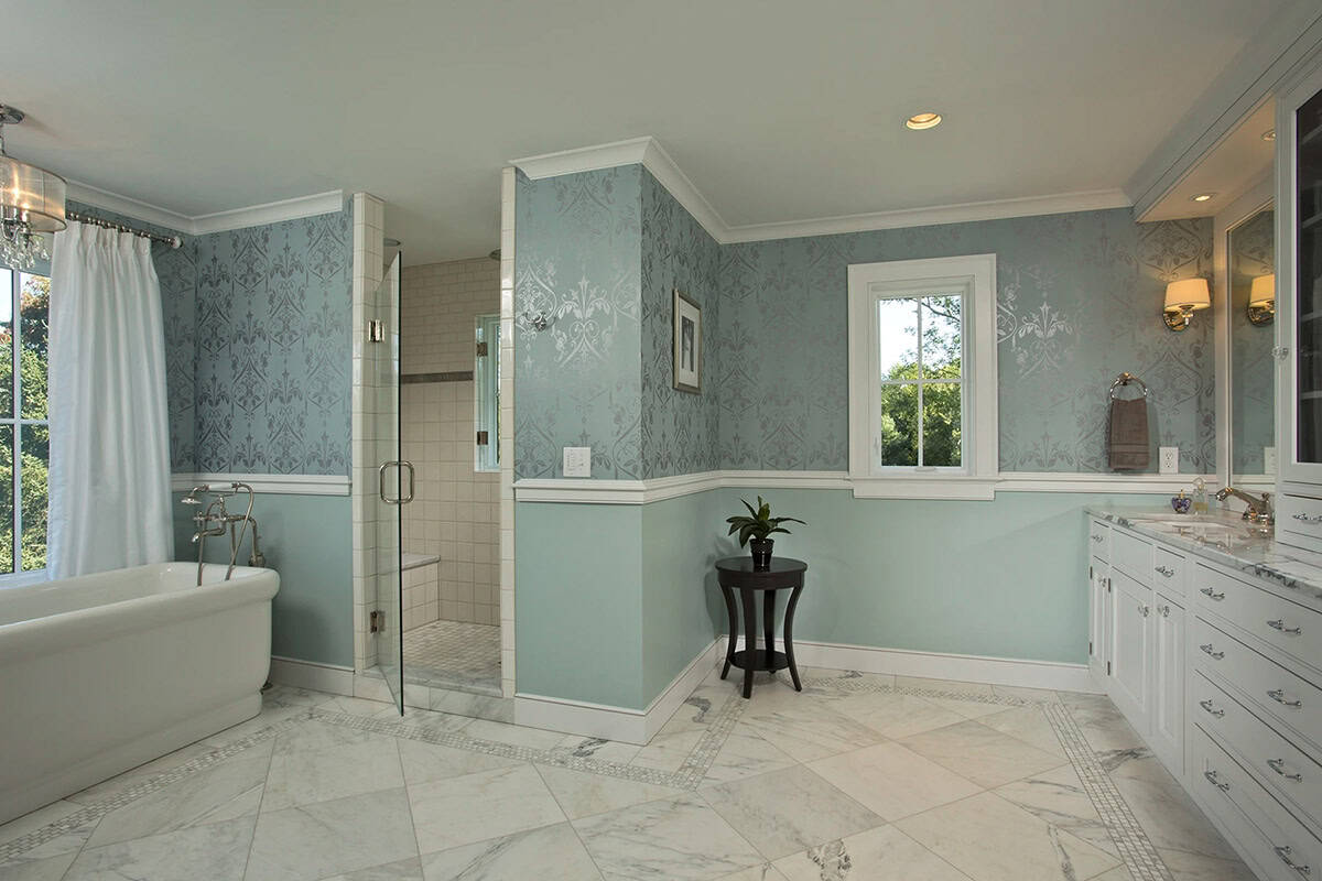 Spacious primary bathroom with freestanding tub, glass shower, marble floors, and blue damask wallpaper