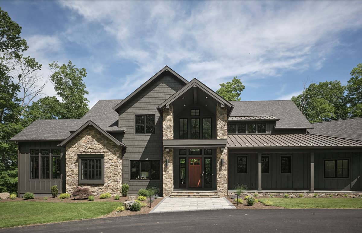Dark gray craftsman home with stone accents, red front door, and wooded setting
