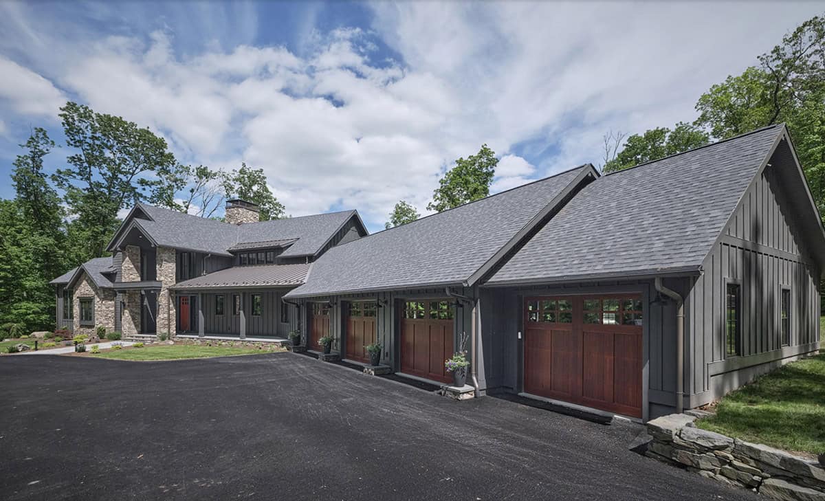 Gray craftsman home with wood garage doors, board and batten siding, and circular driveway