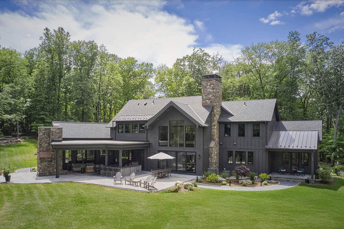 Aerial view of gray craftsman home rear exterior with large patio and wooded backyard