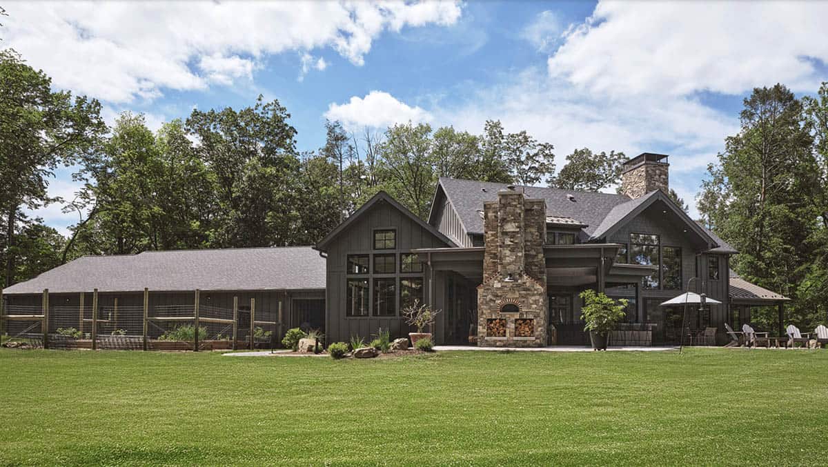 Rear exterior of gray craftsman home with stone chimney, pizza oven, and raised garden beds