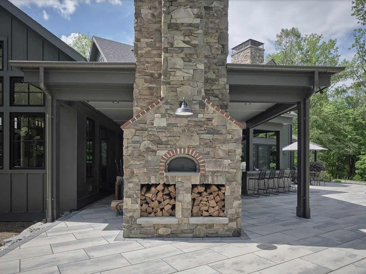 Outdoor stone pizza oven and chimney with covered patio and bar seating beyond