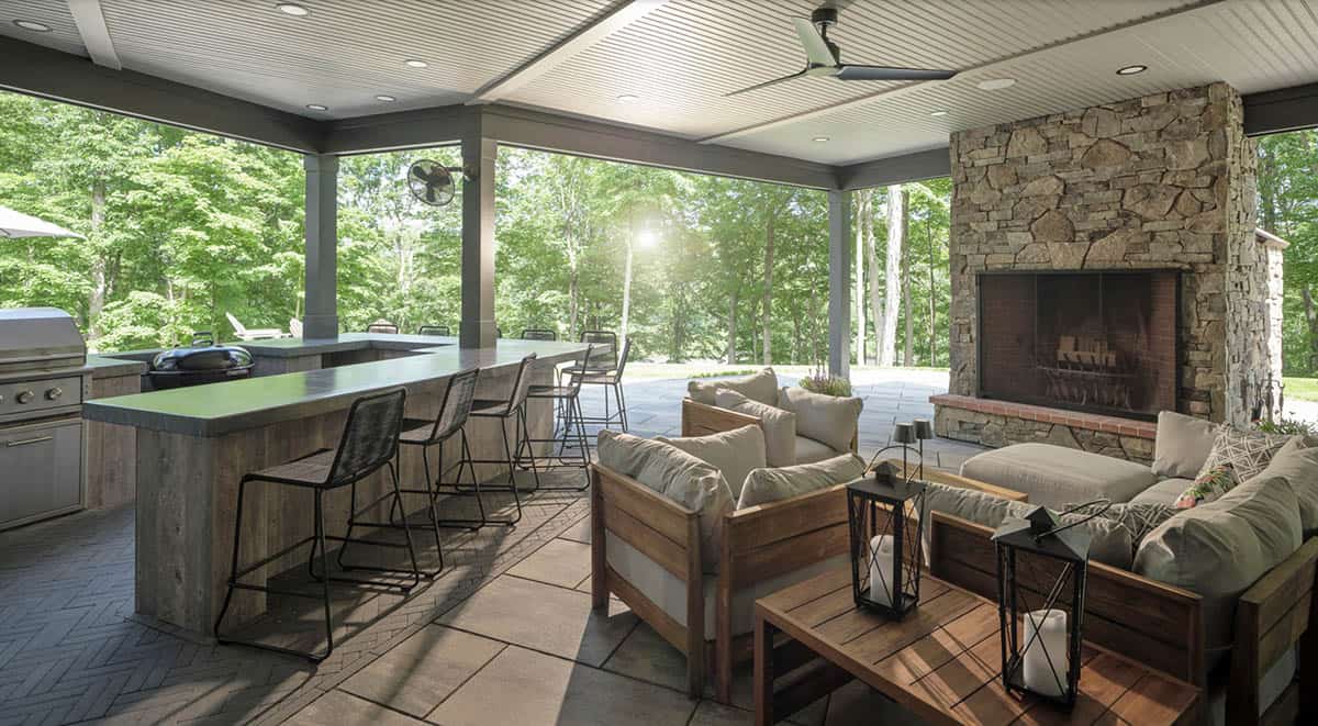 Covered outdoor living area with stone fireplace, kitchen bar, and teak furniture