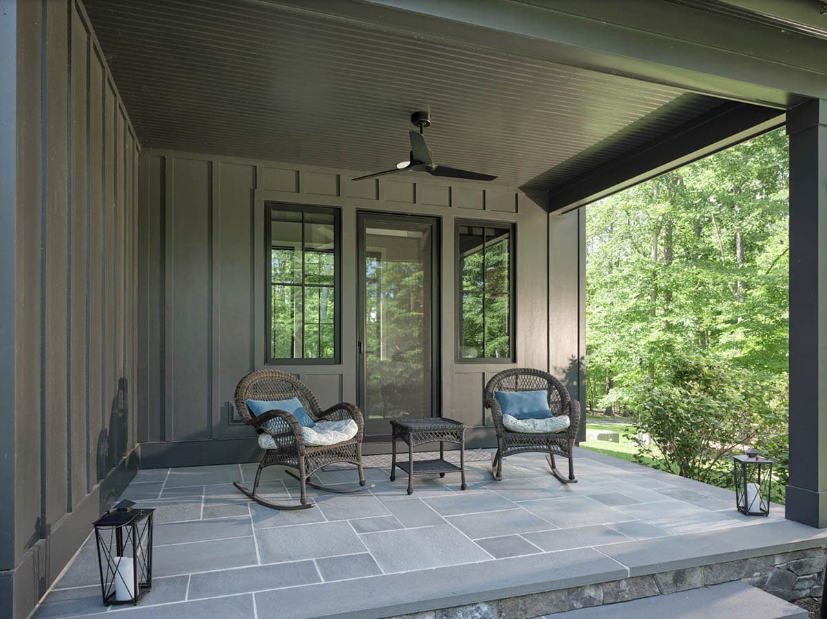 Covered side porch with wicker rocking chairs, slate tile floor, and wooded views