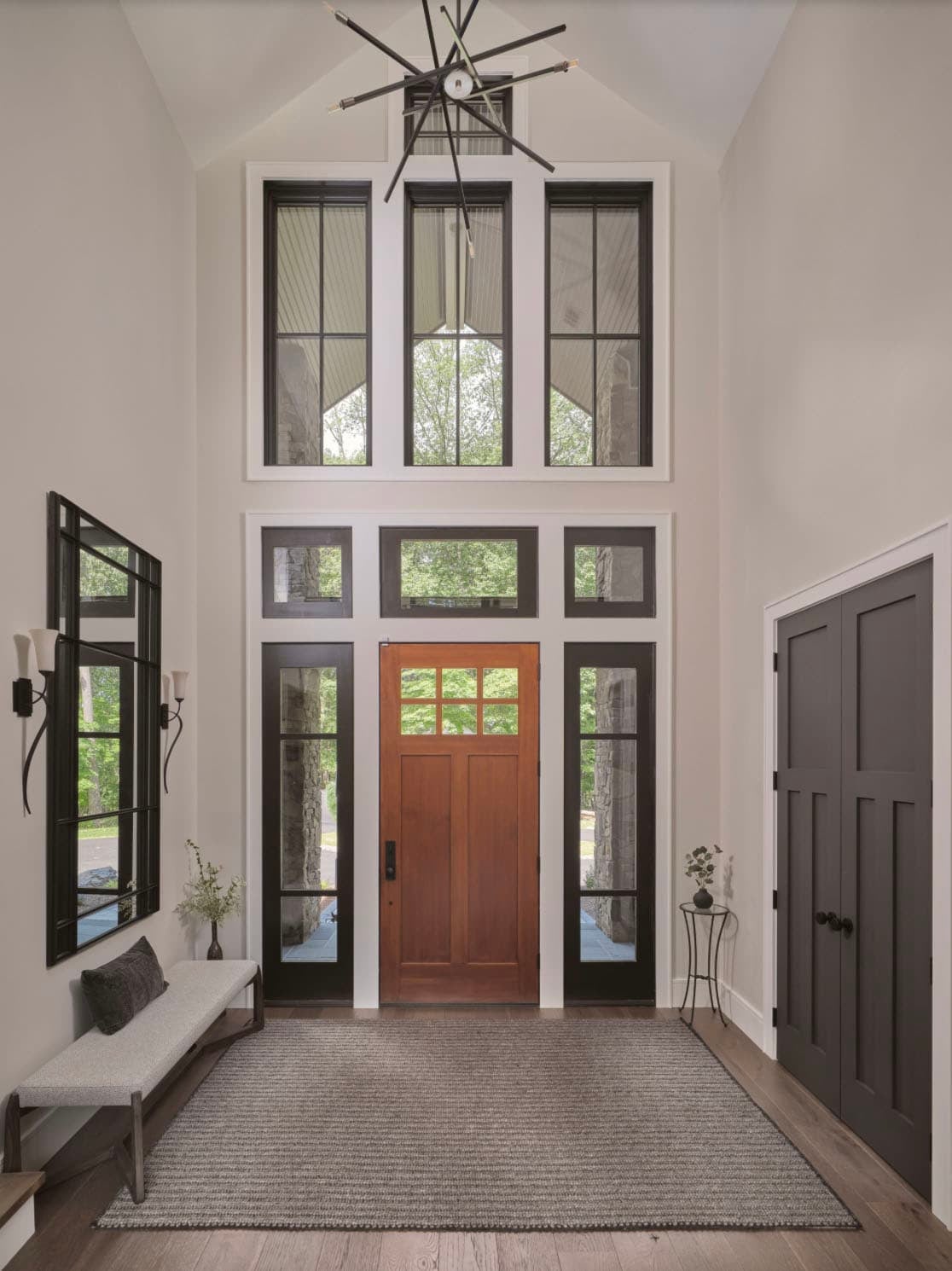 Bright foyer with wood front door, transom windows, sputnik chandelier, and bench seating