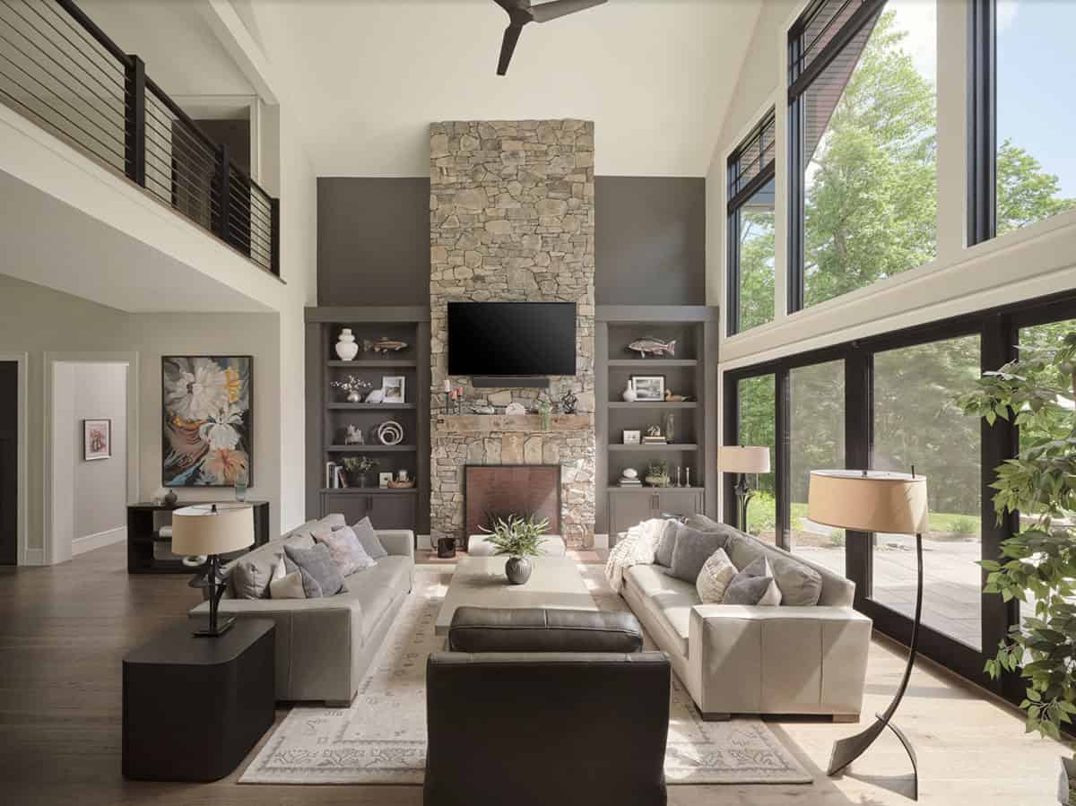 Great room with two-story stone fireplace, built-in shelves, gray sofas, and wall of windows