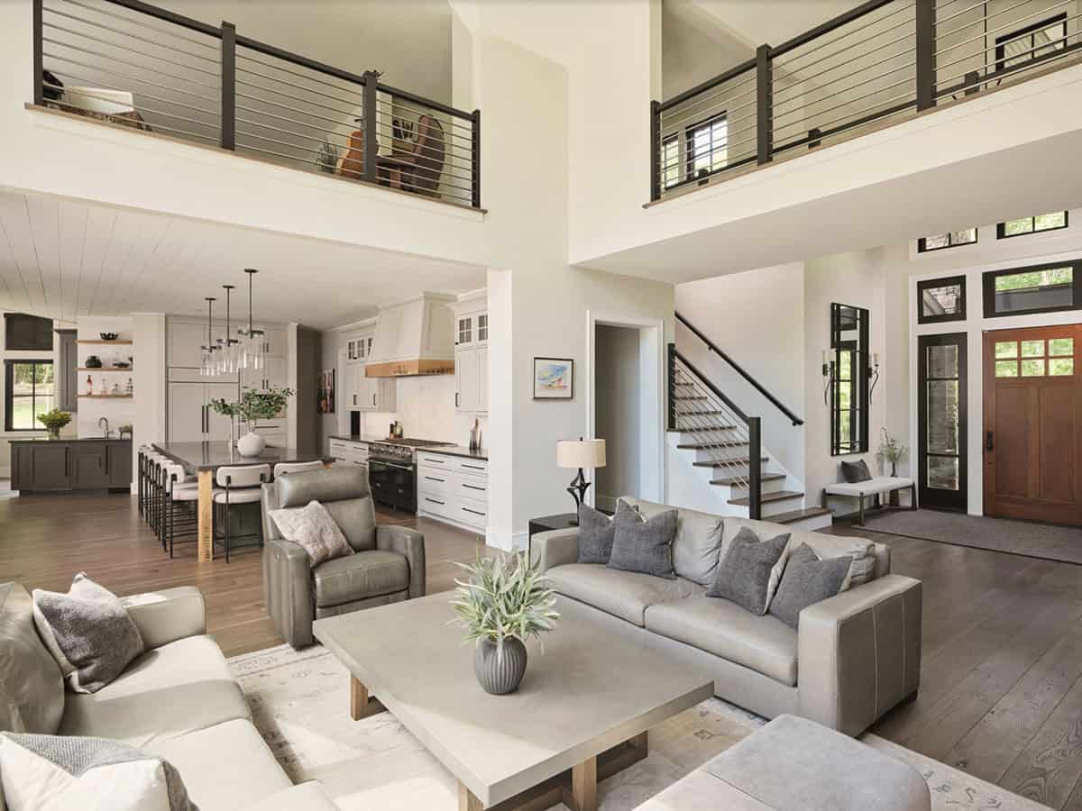 Open plan living area with gray sofas, kitchen beyond, metal railing loft, and wood front door