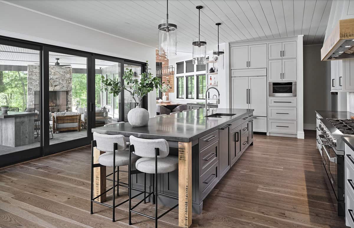 Kitchen with dark gray island, concrete countertop, boucle bar stools, and glass pendant lights