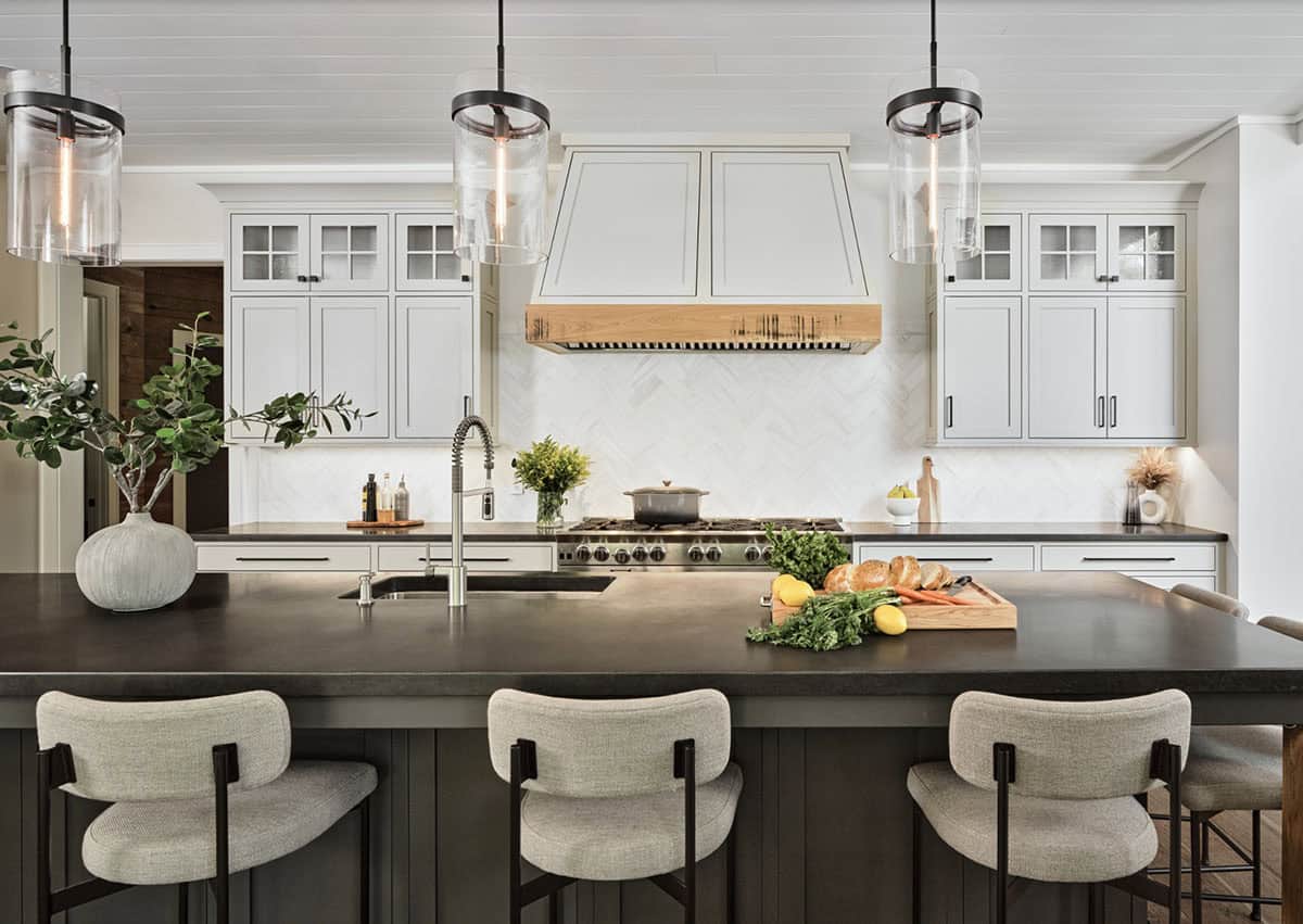 Kitchen with white cabinetry, wood-trimmed range hood, herringbone backsplash, and dark island