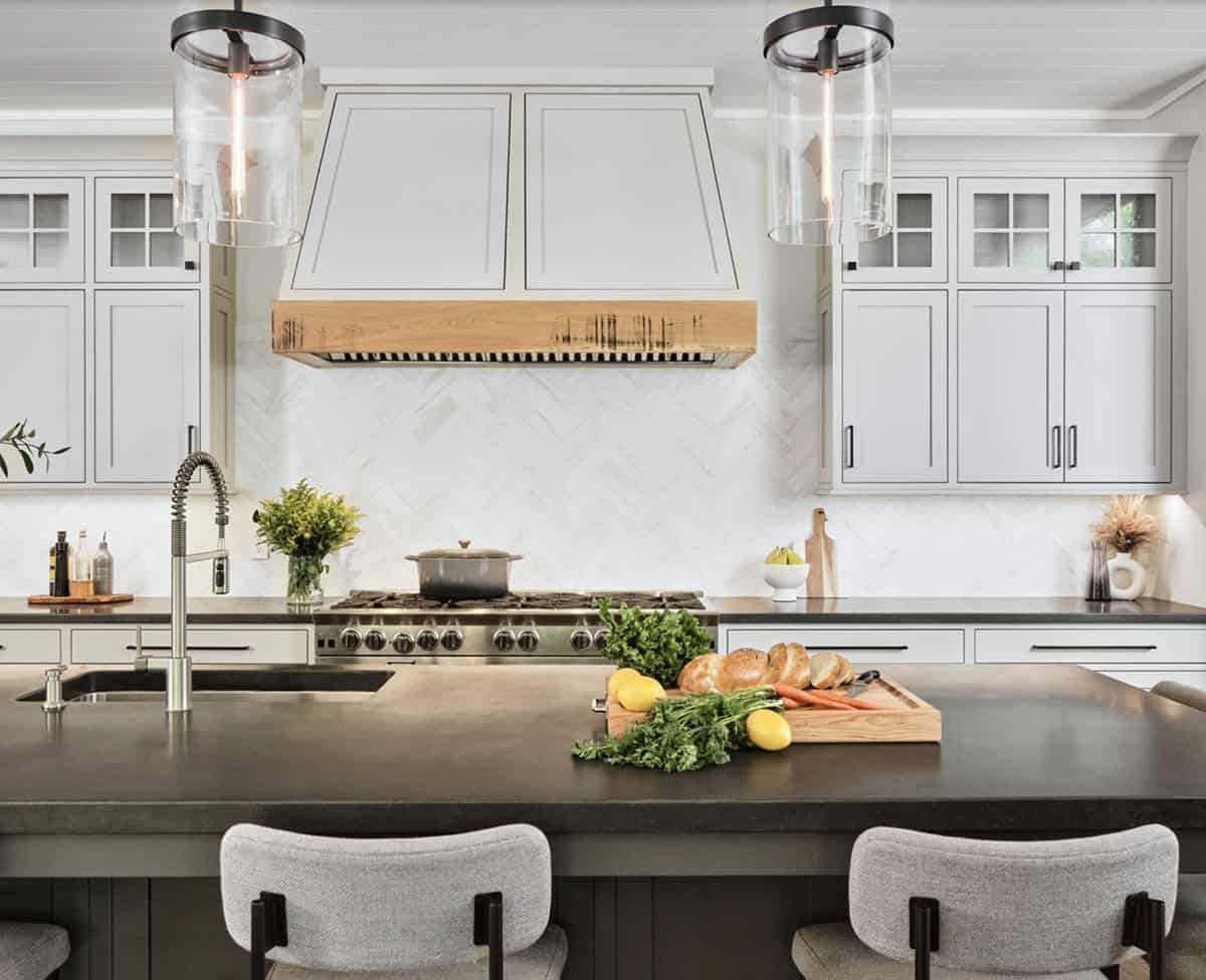 Close-up of kitchen range hood with raw wood trim, herringbone backsplash, and professional range