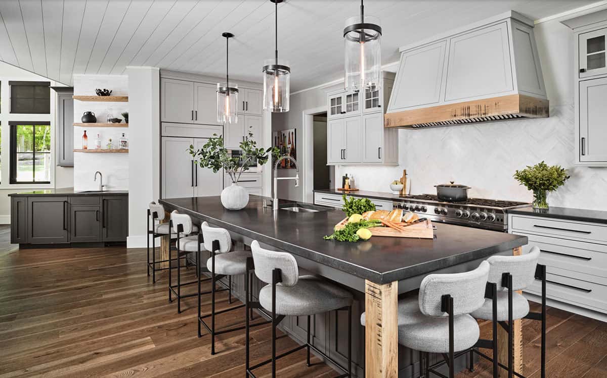 Large kitchen island with dark countertop, boucle stools, pendant lights, and herringbone backsplash
