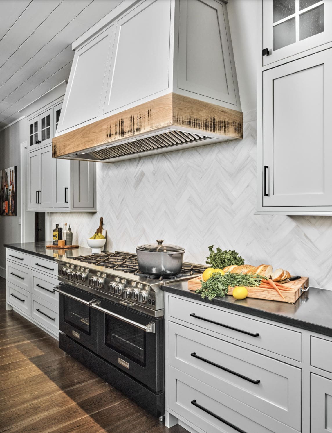 Close-up of professional range with wood-trimmed hood, herringbone tile backsplash, and dark countertops