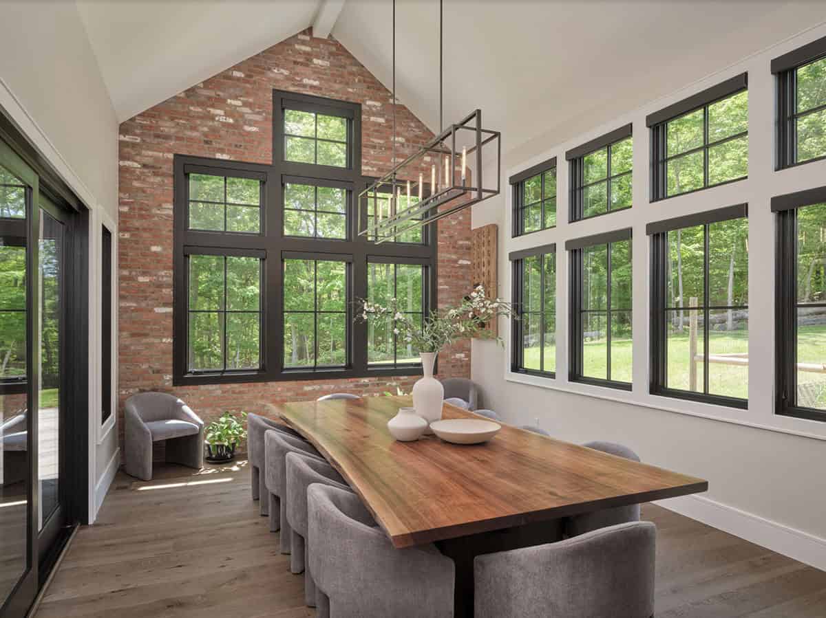Dining room with live edge wood table, exposed brick wall, black windows, and linear chandelier