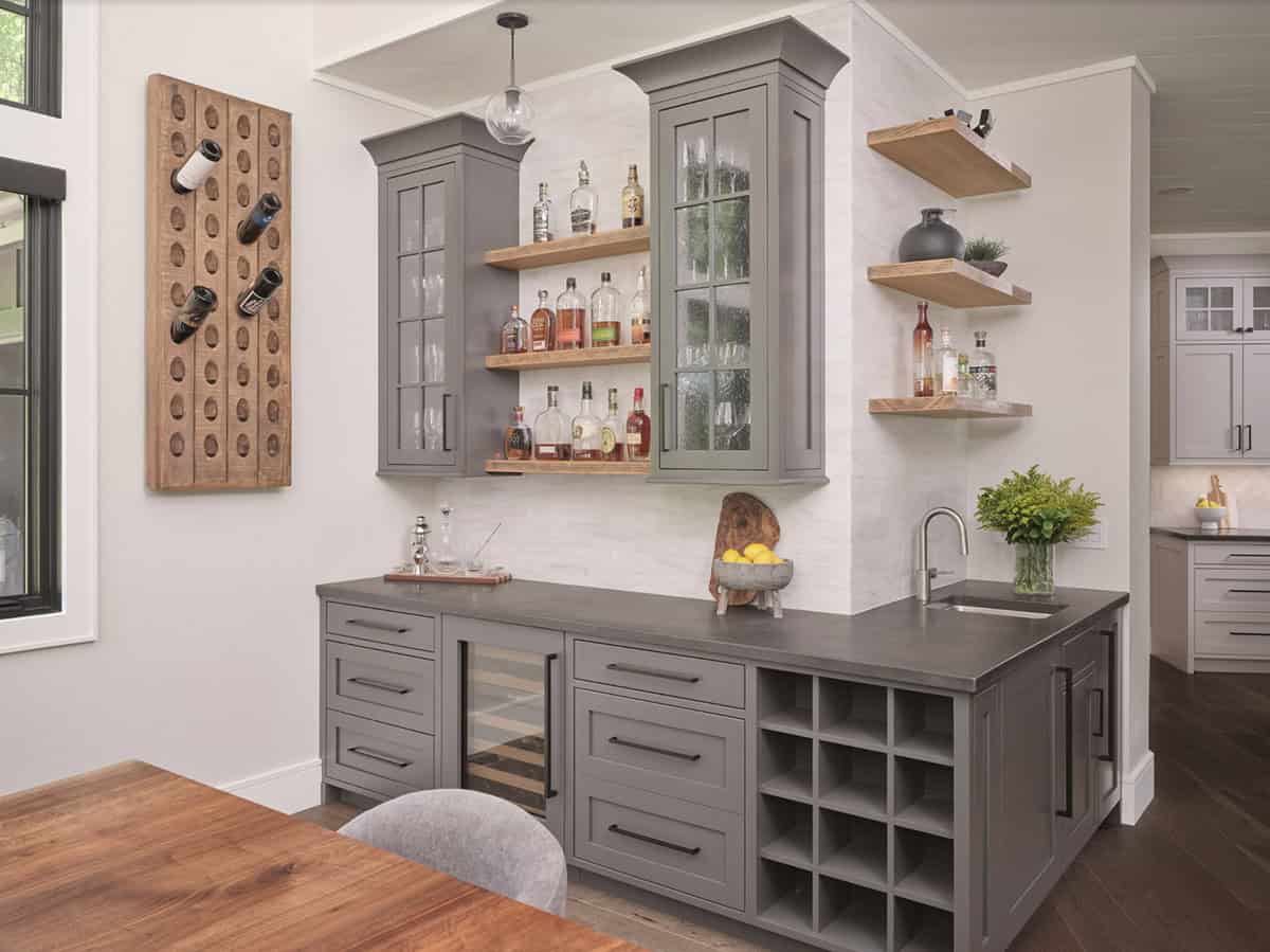 Gray wet bar with wine fridge, open shelving, bottle storage, and rustic wine rack wall art
