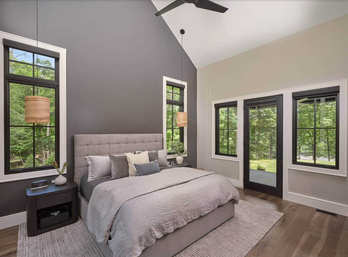 Primary bedroom with dark accent wall, vaulted ceiling, wood pendant lights, and wooded views