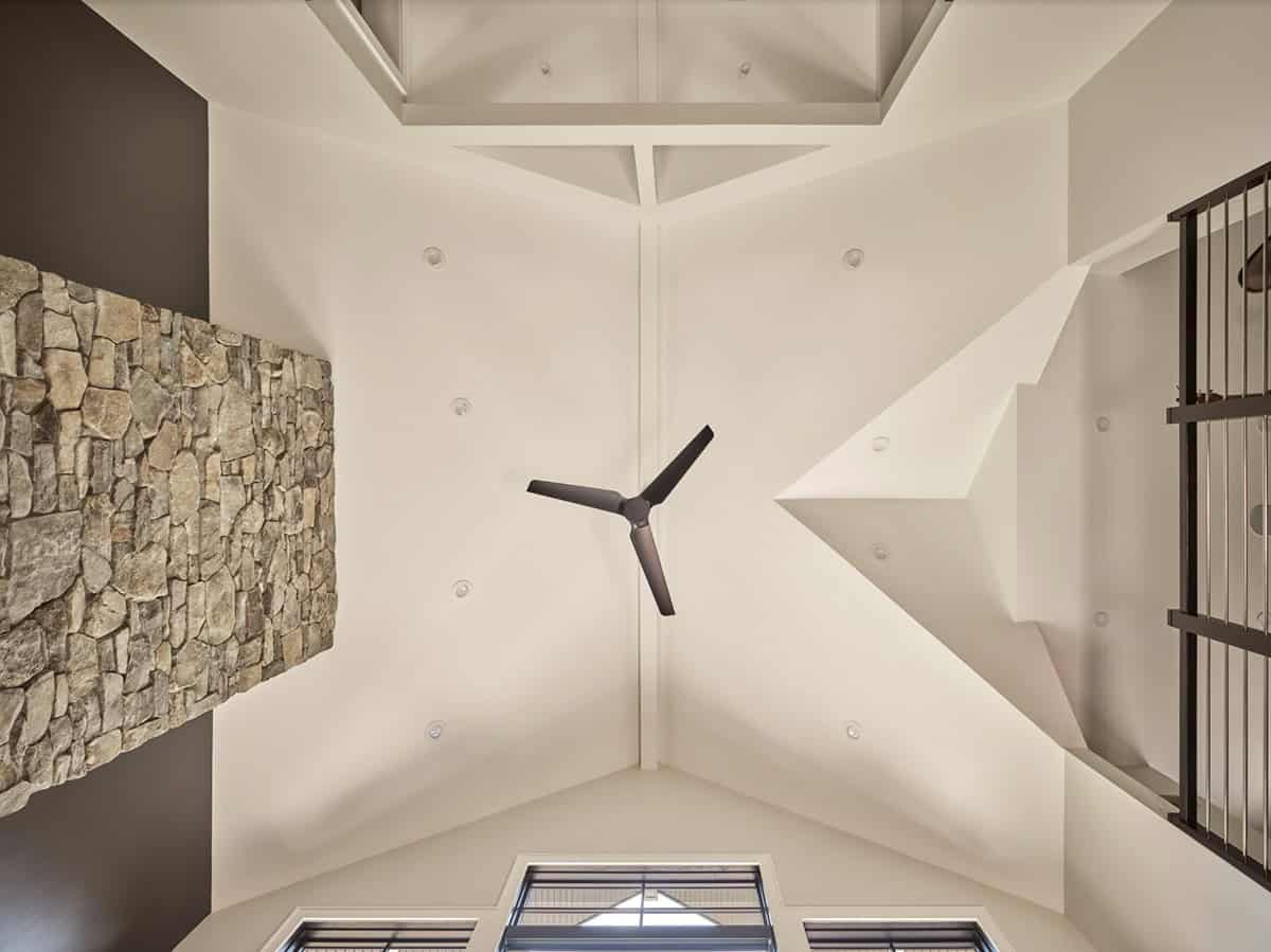 Looking up at vaulted ceiling with stone chimney, ceiling fan, and metal railing loft