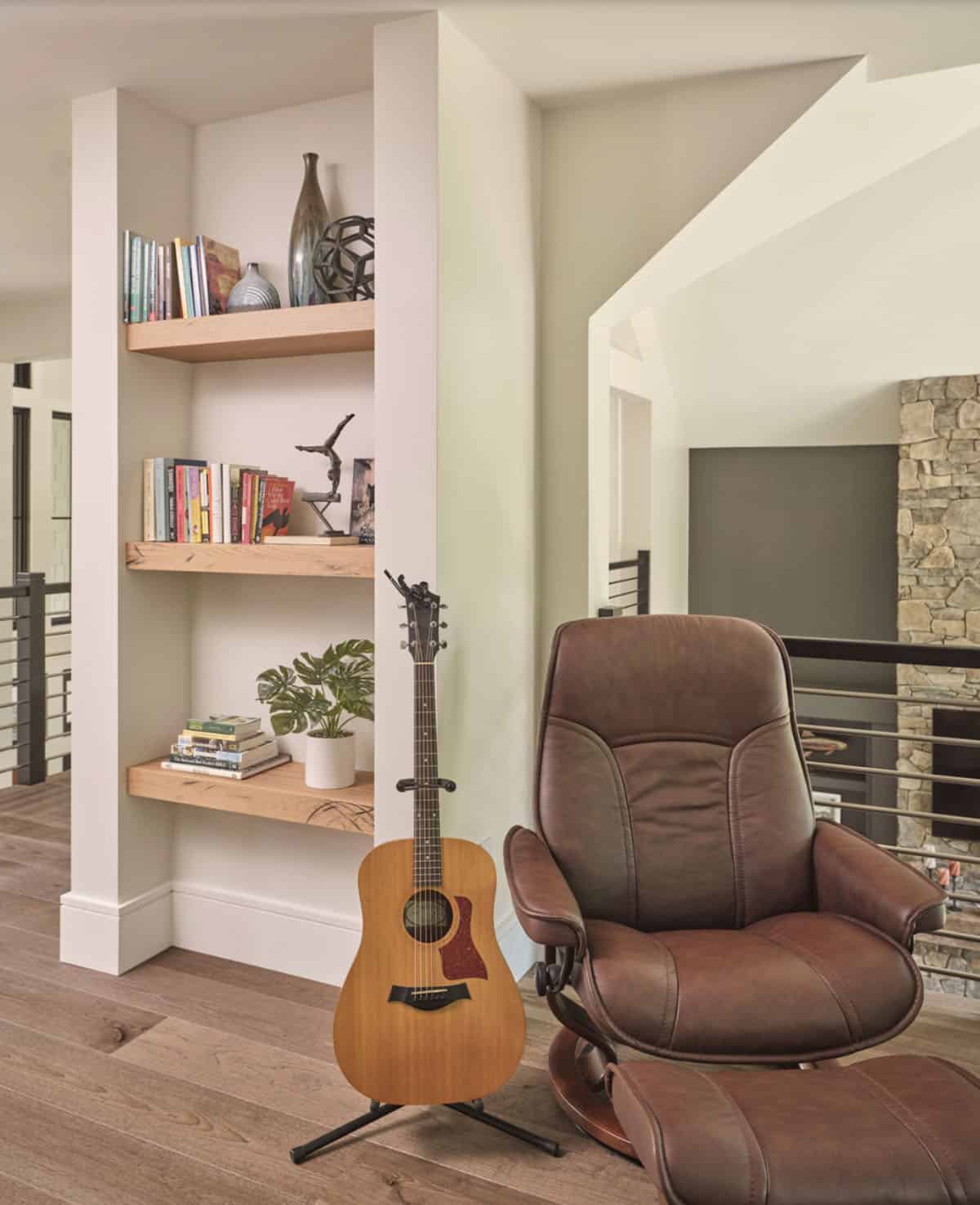 Loft reading nook with built-in oak shelves, leather recliner, and guitar