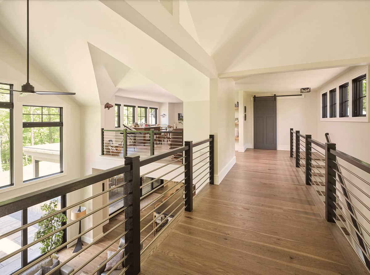 Second floor hallway with metal railings, barn door, vaulted ceiling, and wooded views
