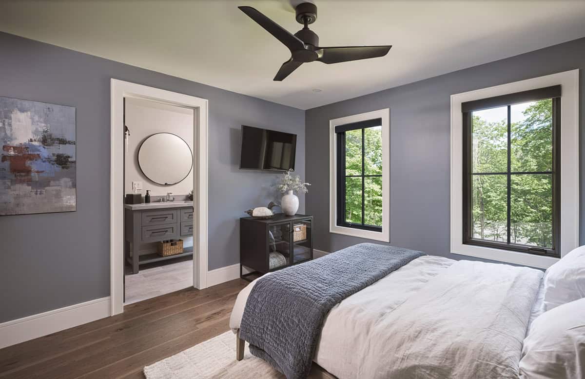 Guest bedroom with blue-gray walls, black windows, wooded views, and en suite bathroom