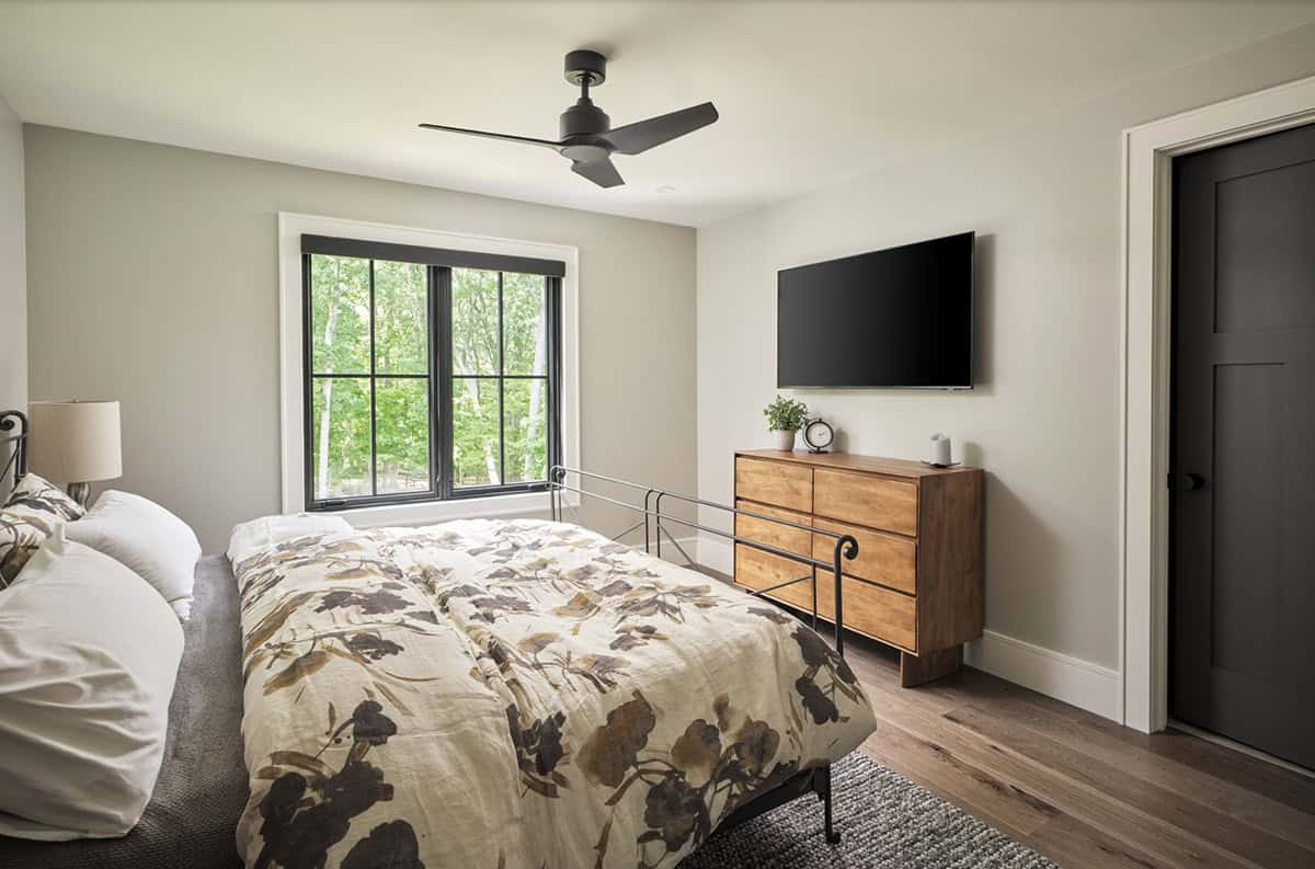 Guest bedroom with floral bedding, iron bed frame, wood dresser, and black window