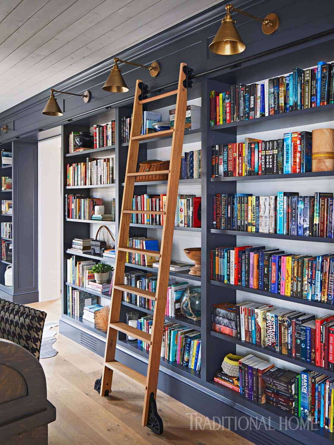 Floor-to-ceiling dark blue built-in bookshelves with rolling library ladder and brass wall sconces