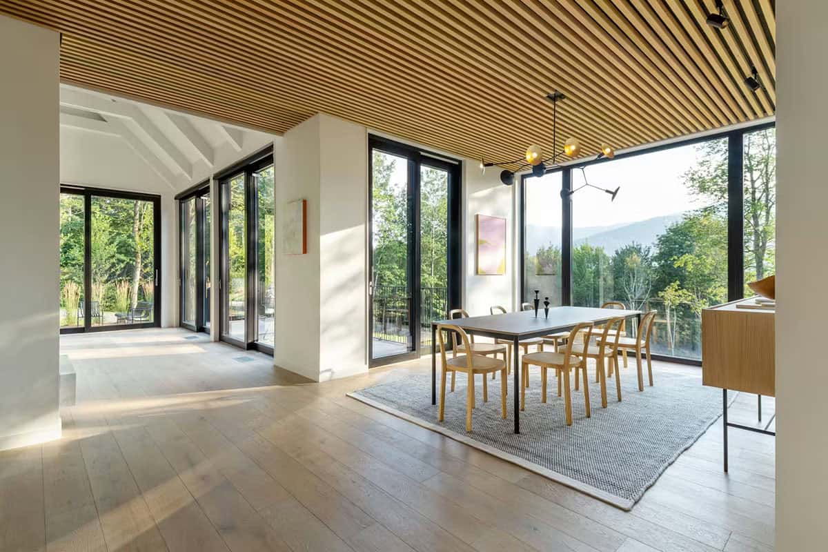 Modern farmhouse open plan dining room with wood slat ceiling, floor-to-ceiling European windows and Green Mountain views in Vermont