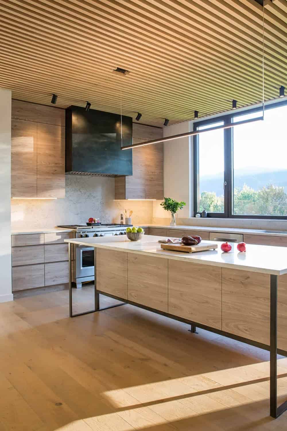 Modern farmhouse kitchen with wood veneer cabinetry, blackened steel range hood, wood slat ceiling and Green Mountain views in Vermont