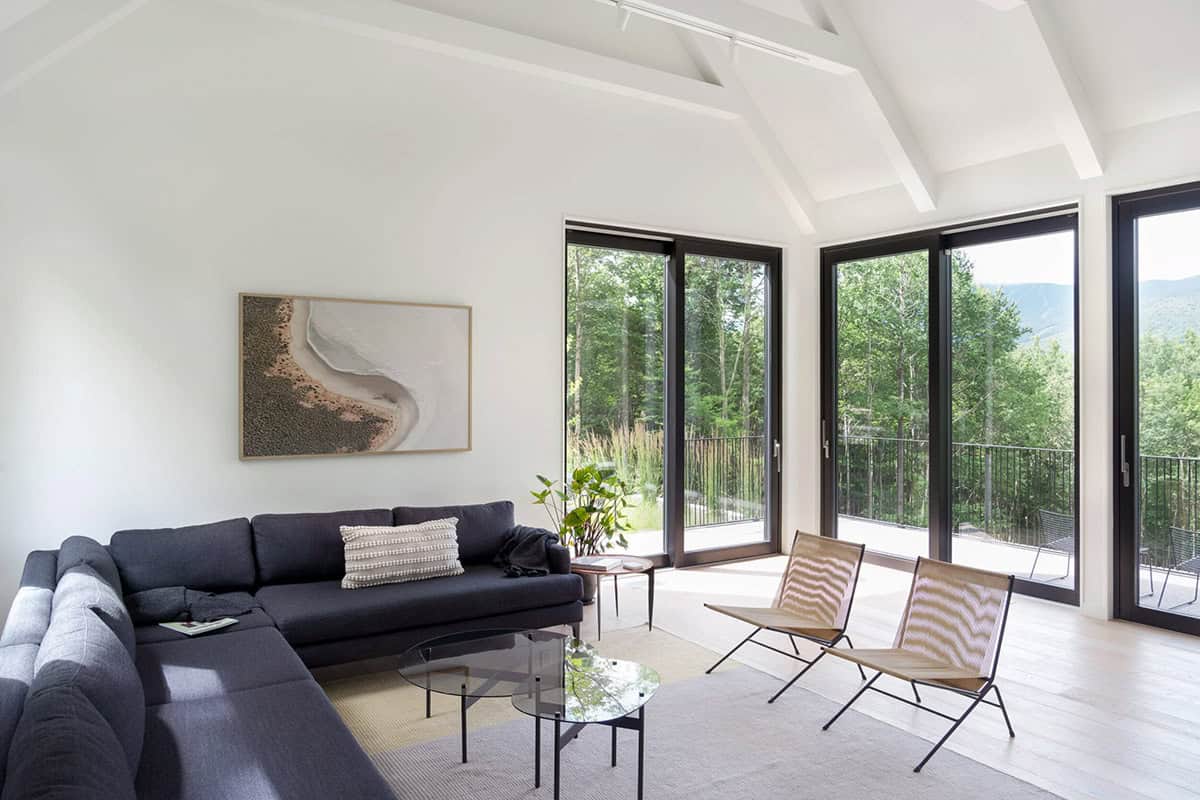 Modern farmhouse living room with vaulted ceiling, large European windows and balcony with Vermont woodland views 
