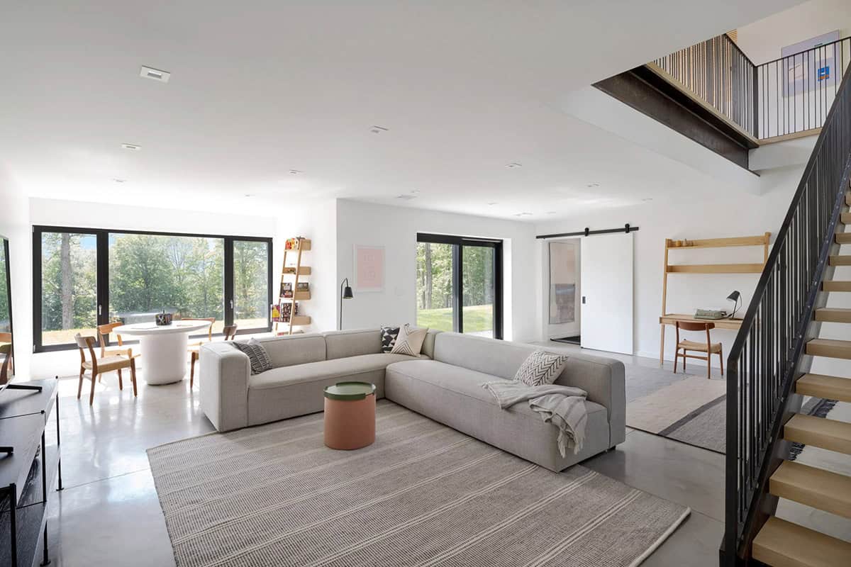 Modern farmhouse open plan lower level living room with steel staircase, barn door, concrete floors and woodland views in Vermont 
