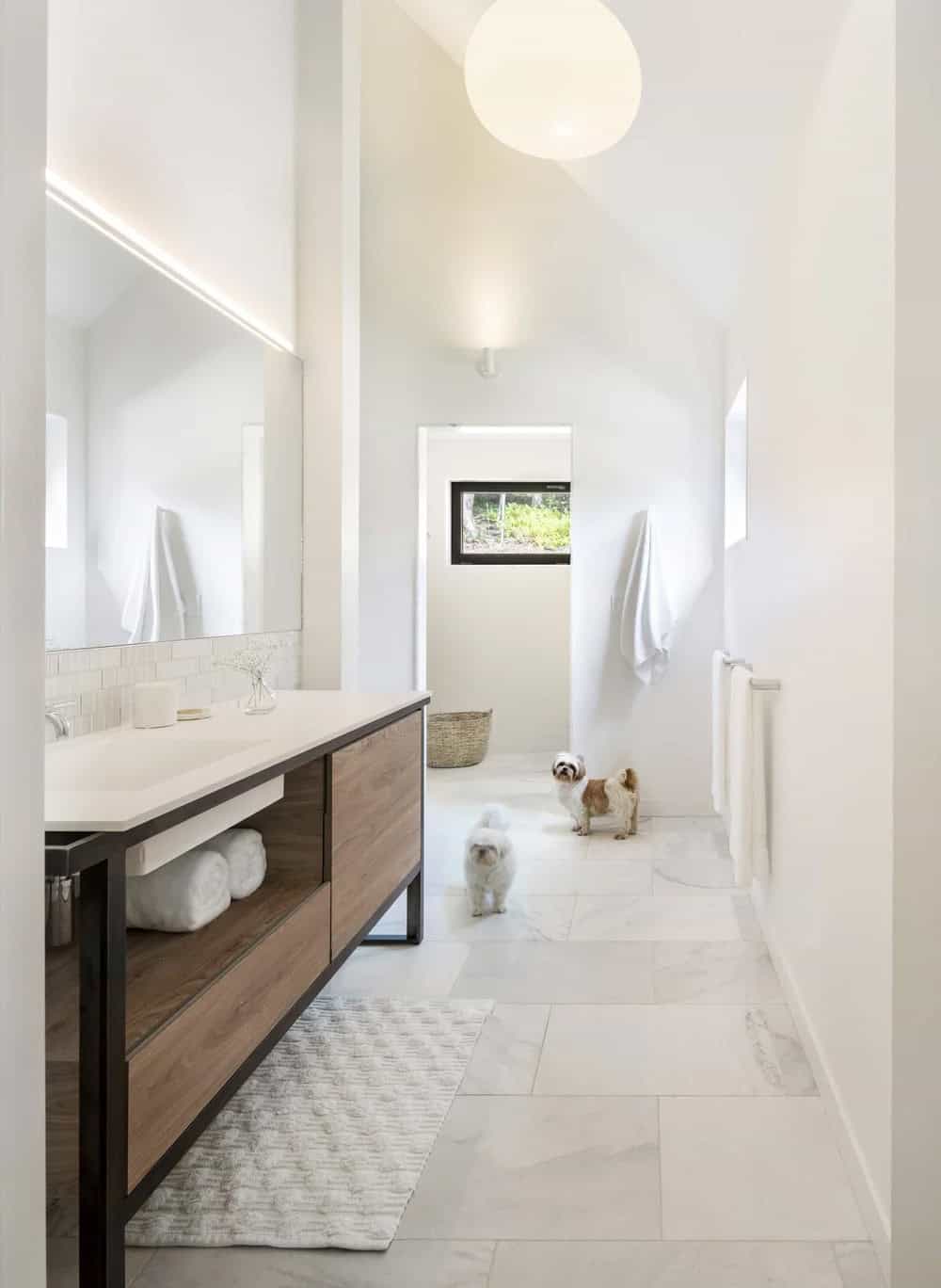 Bright modern farmhouse primary bathroom with wood and steel vanity, marble tile floor and vaulted ceiling in Vermont