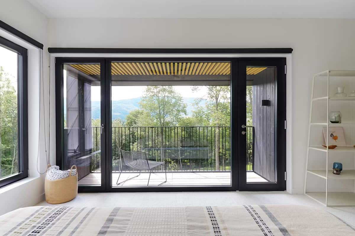 Modern farmhouse bedroom with floor-to-ceiling glass doors opening to a private balcony with Green Mountain views in Vermont