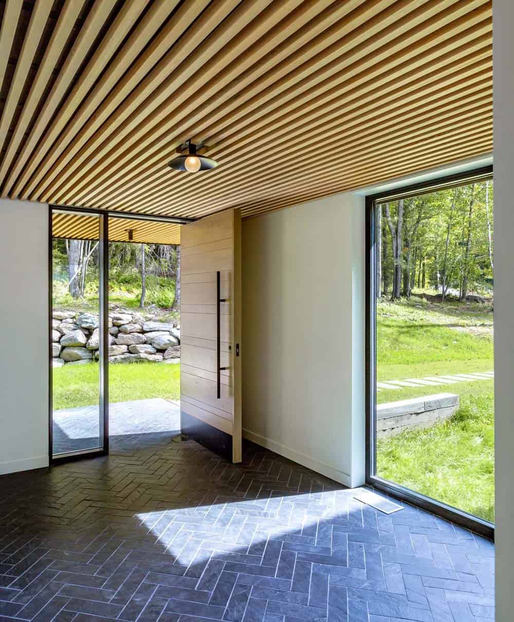 Modern farmhouse entry with oversized oak pivot door, herringbone slate tile floor and wood slat ceiling in Vermont
