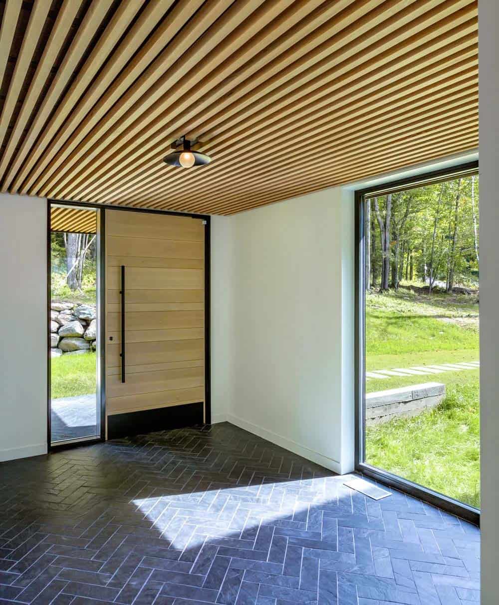 Modern farmhouse glassy entry node with oak pivot door, herringbone slate floor and hemlock wood slat ceiling in Vermont